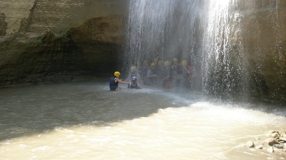 Travelers standing under a waterfall inside a cave-like chamber of Osumi Canyon